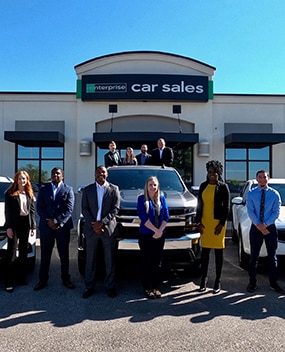 Group of employees with vehicles in front of a car sales office